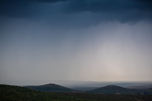 灰色的暴风雨天空的图像和雨在山上和田野在远处。库存图片图片下载
