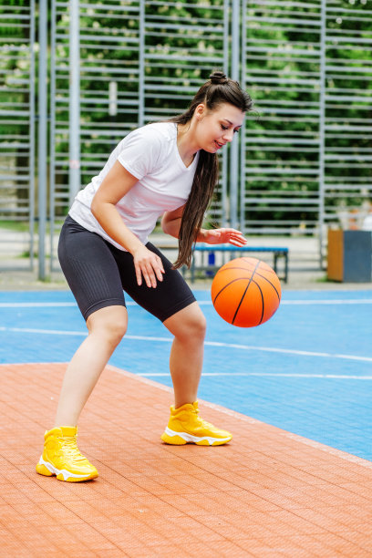 年轻的女运动员正在现代户外篮球场训练打篮球。快乐的女人图片下载
