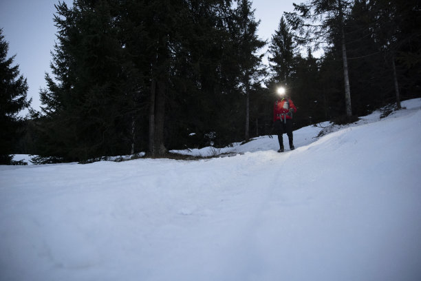 徒步旅行者在黄昏时带着头灯走在雪地上。图片下载