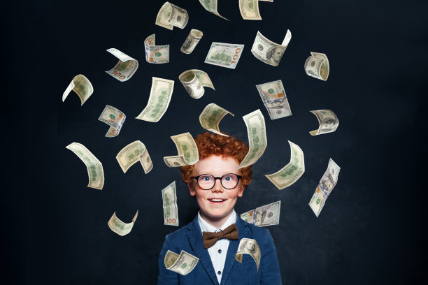 快乐的红发小男孩站在钱雨下，对着黑板墙的背景图片下载