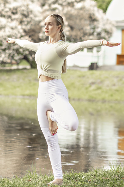 一个年轻美丽、苗条的金发女孩夏天在公园池塘边的自然中做瑜伽。图片下载