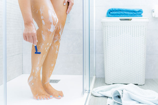 一个女人在淋浴间用剃刀刮腿毛图片下载