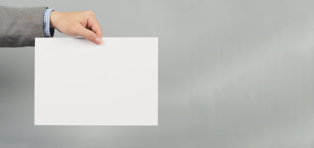 双手拿着灰色背景的空白白色A4纸。穿灰色西装。商人的概念。图片下载
