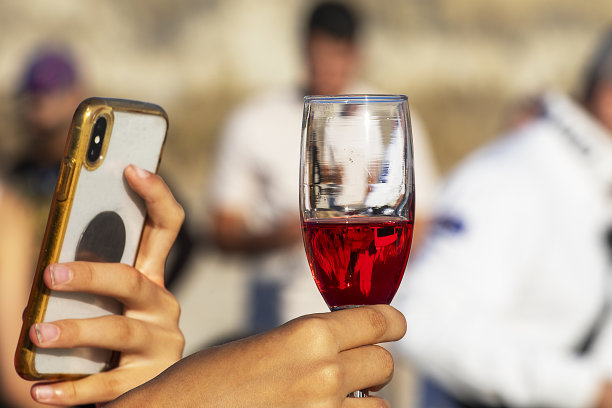 在一场青年派对上，拿着盛满红色香槟的玻璃杯，用手机自拍。假期图片下载