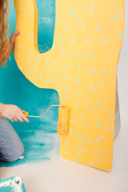 可爱的小女孩在公寓里修理房子，粉刷墙壁。一个美丽微笑的孩子的肖像与油漆辊和大纸仙人掌在工作室。欢快可爱的宝宝玩得很开心图片下载