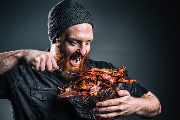 大胡子男人正用叉子吃着一碗培根图片下载