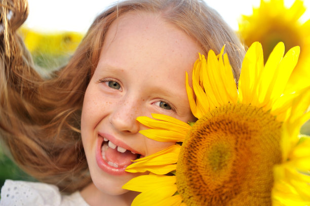一个笑着拿着向日葵的女孩的特写肖像对着她的眼睛图片下载