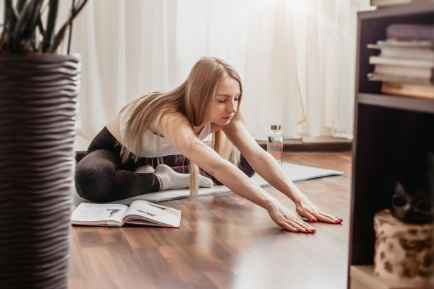 瑜伽在家里。年轻的金发女子坐在家里地板上的瑜伽垫上做普拉提和瑜伽练习。伸展运动。图片下载