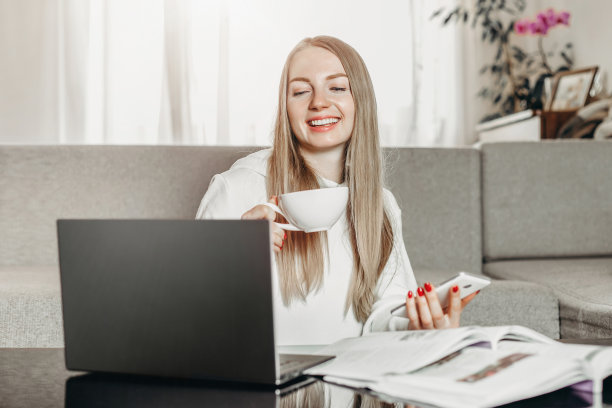 年轻的女学生坐在家里，拿着笔记本电脑、手机和课本在网上学习英语图片下载