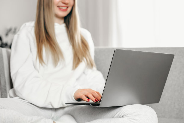 一个年轻的金发女郎坐在沙发上用她的笔记本电脑。远程教育。在线工作。自由职业者的女孩图片下载