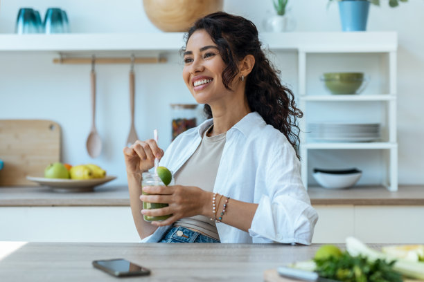 漂亮女人在家里的厨房里喝着水果排毒果汁，眼睛斜视着。图片下载