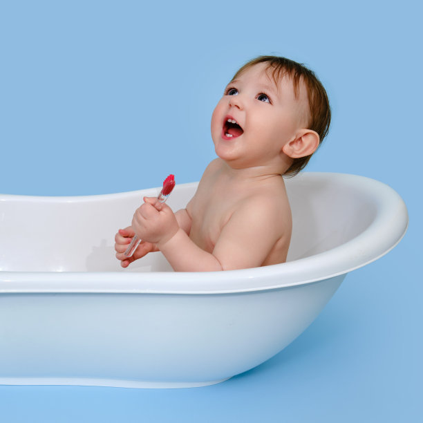 快乐的婴儿蹒跚学步的男孩与牙刷在一个白色浴缸在工作室的蓝色背景。一岁的微笑的孩子图片下载