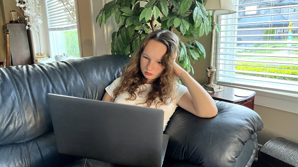 在线学习金发欧洲女孩坐在她的膝盖上，在阳台上的街道上用笔记本电脑或观看一节课。在她的手边有一张打印出来的纸，她将在上面完成任务。图片下载