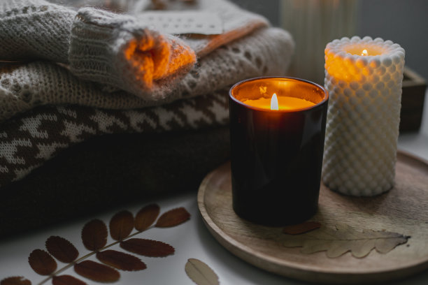 两支燃烧的蜡烛和一叠温暖舒适的毛衣放在床上。家里舒适的秋夜图片下载