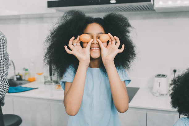 孩子拿着鸡蛋在他的眼睛附近，在厨房做饭。孩子们娱乐。健康饮食的概念图片下载