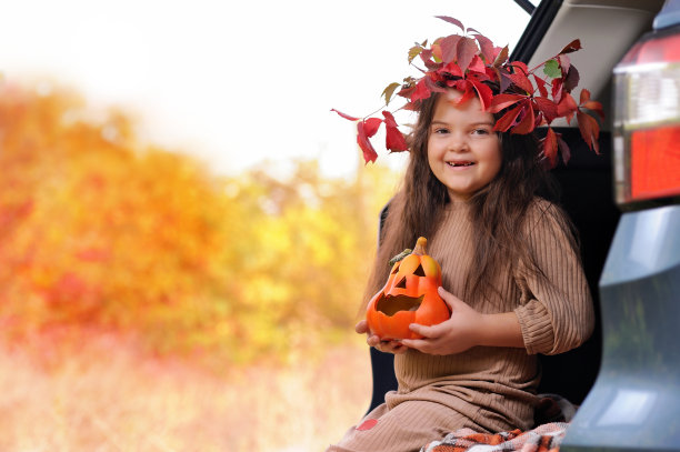 快乐的女孩带着秋天的花环在汽车后备箱里图片下载