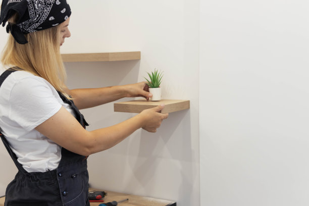 一个穿着白色t恤和工作服的金发女孩把一朵绿色的花放在一个白色的花盆里，在一个棕色的小架子上，有一个地方写着碑文。高质量的照片图片下载