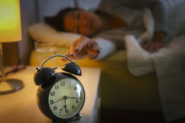 女人在床上摸到床头柜上的闹钟图片下载
