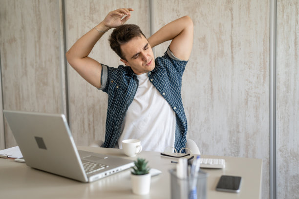 年轻人坐在办公桌前做伸展运动时背部疼痛图片下载