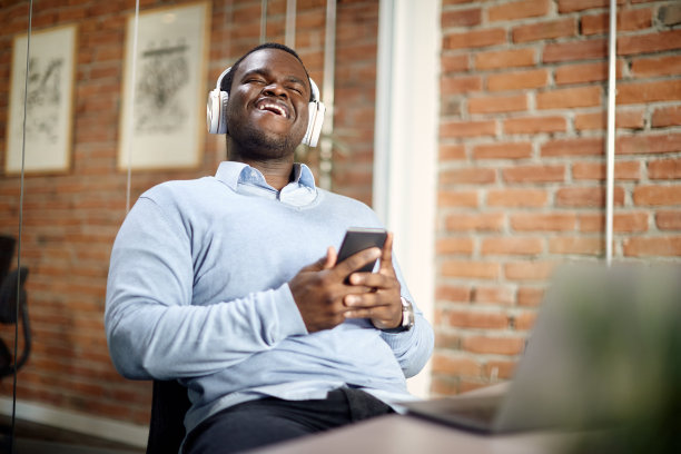 快乐的黑人商人在办公室用手机和耳机享受音乐。图片下载