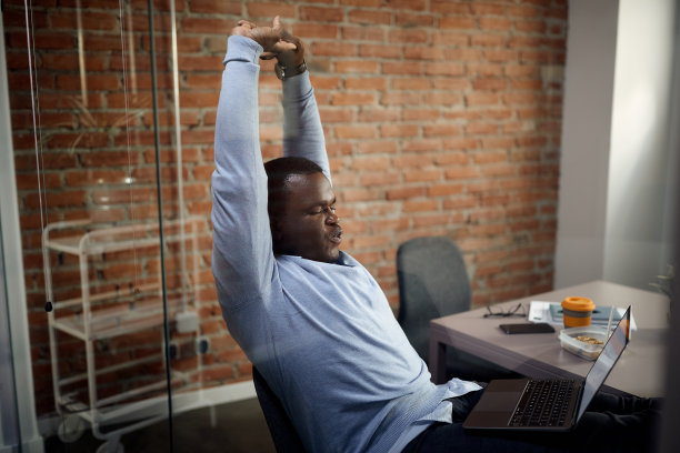 黑人商人在办公室电脑前做伸展运动。图片下载