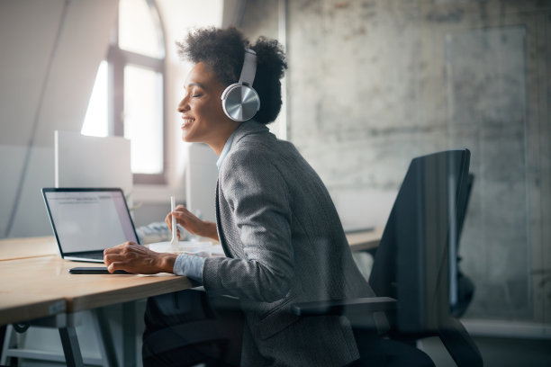 快乐的黑人女商人享受音乐耳机，而在午休的工作。图片下载