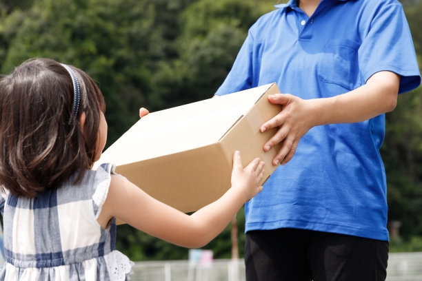 一位送快递的妇女把包裹递给一个孩子。儿童食品配送服务企业的图片。图片下载