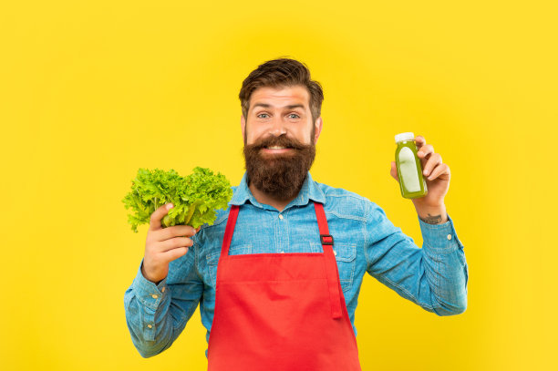 快乐的男人穿着围裙，手里拿着新鲜的生菜和橙汁，底色黄色，多汁图片下载