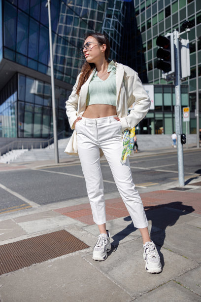 迷人的女人穿着时髦的衣服站在摩天大楼的城市景观背景，看着别处图片下载