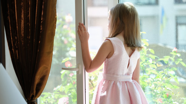 小女孩站在家里开着的窗户前看后景图片下载