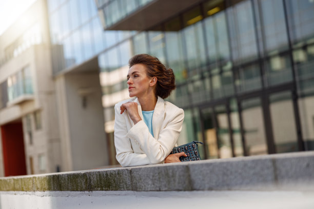 专注的白色西装女士站在商业中心附近。模糊的背景图片下载