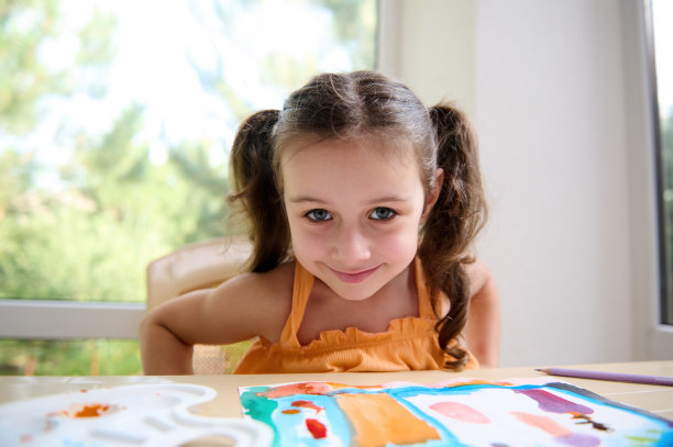 可爱的小女孩和两个有趣的马尾辫坐在桌子与她的画，在水彩画艺术课上图片下载