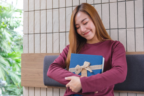 一名年轻女子闭着眼睛接受并拥抱一个礼物盒的肖像形象图片下载