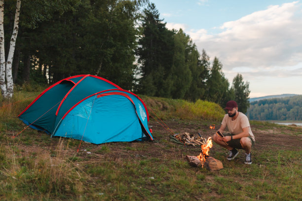 一名年轻人在户外露营时在帐篷外燃起营火图片下载