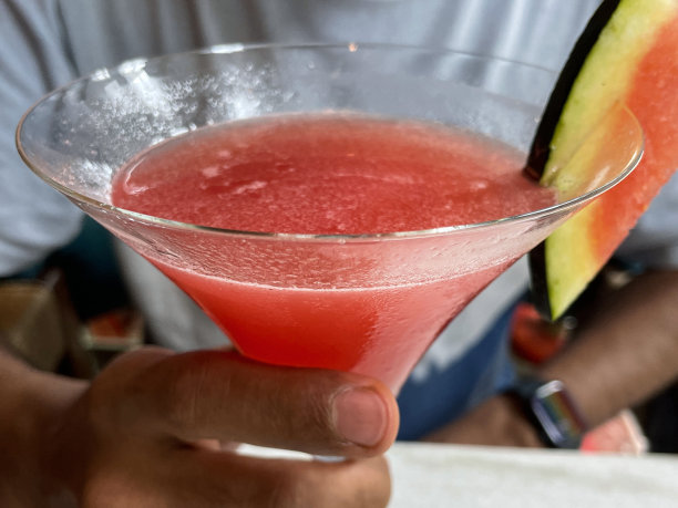特写的餐厅场景的桌子上，面面相觑的人拿着马提尼杯的西瓜鸡尾酒和西瓜片，喝酒精伏特加为主的饮料图片下载