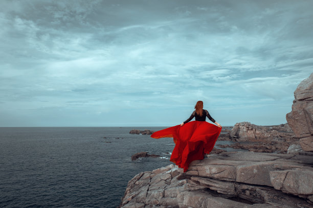 一个红头发的人穿着优雅的红色长裙在戏剧性的风景中摆姿势图片下载