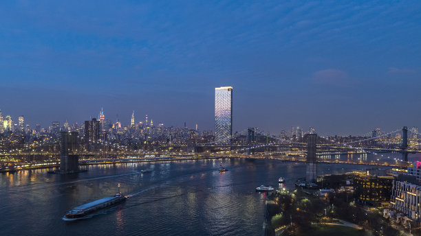 船在布鲁克林大桥和曼哈顿大桥前沿着东河航行，在夜晚的灯光下，穿过东河，连接着布鲁克林和曼哈顿。图片下载