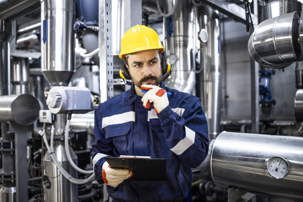 在炼油厂的天然气管道前，白人工人站在深思熟虑的肖像。图片下载