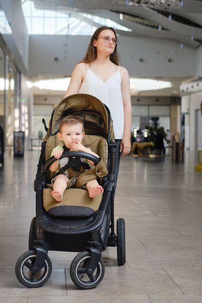 一位母亲和一个坐在婴儿车里的孩子站在一家购物中心的商店外面。妈妈带着一个蹒跚学步的小男孩购物图片下载
