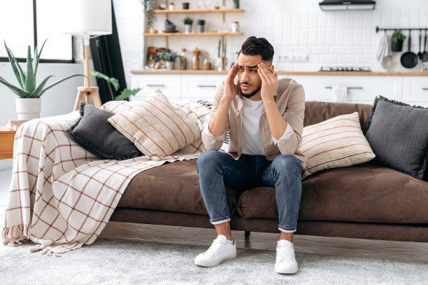 悲伤的阿拉伯人或印度人，坐在客厅的沙发上，专注于个人问题，被坏消息悲伤，经历抑郁，绝望，头痛，偏头痛，需要休息和心理支持图片下载