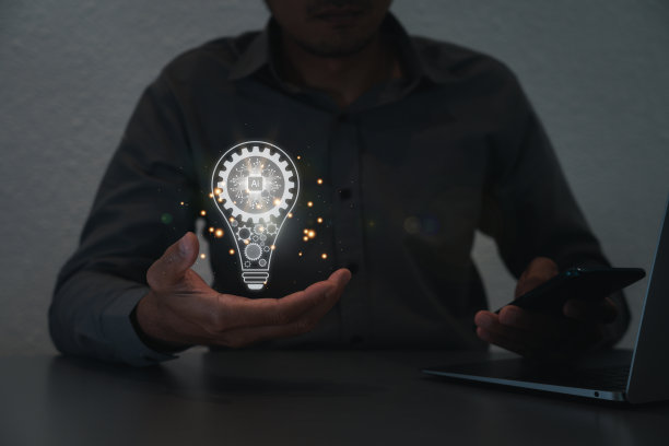 一个男人的手拿着一个灯泡，里面有一个齿轮图标，他在用笔记本电脑。灵感来自在线技术。创新理念的概念。图片下载