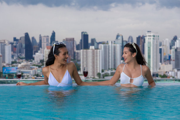 一群亚洲朋友在泳池派对上谈笑风生，眺望着美丽的城市景色。图片下载