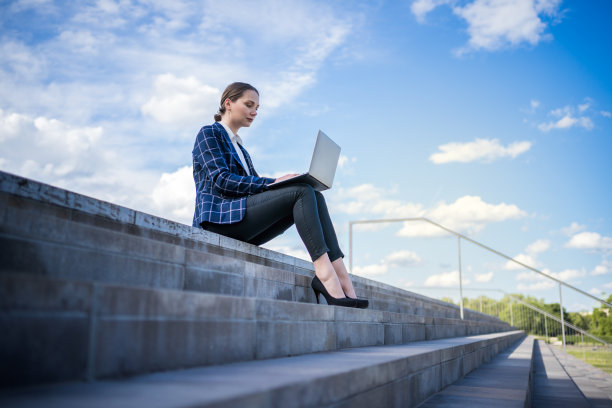 穿着得体的年轻女商人带着上网本坐在台阶上，在现代城市的街道上工作图片下载