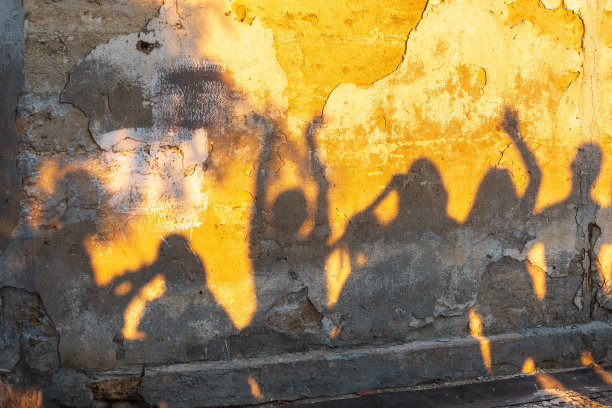 日落时分，老石墙上跳舞的人的影子。图片下载