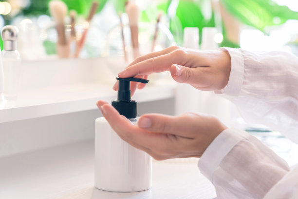 坐在化妆用品和镜子的梳妆台旁边的女人在手上涂daily cream。图片下载