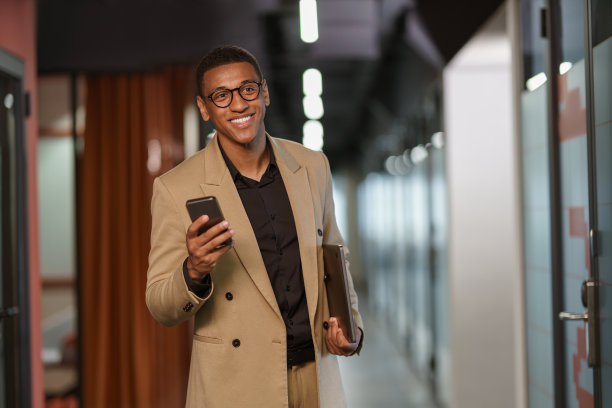 英俊微笑的非洲商人使用电话，而站在现代联合工作图片下载