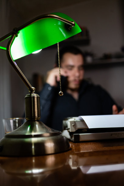 一个年轻人在长时间的工作后，晚上在他的家里在他的办公室打电话。图片下载