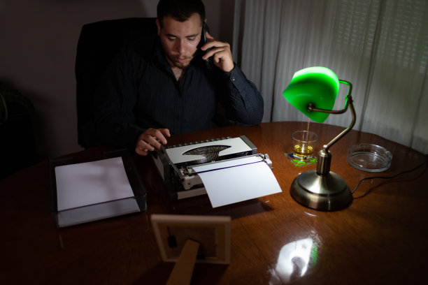 一个年轻人在长时间的工作后，晚上在他的家里在他的办公室打电话。图片下载