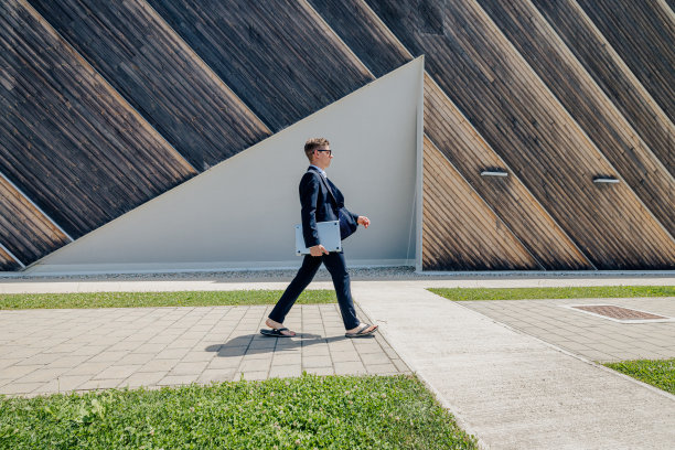 侧视图的商业专业人士步行与笔记本电脑在人行道靠墙图片下载