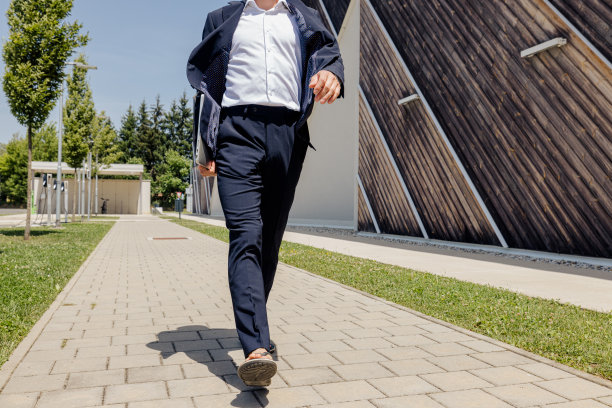 自信的专业人士带着笔记本电脑走在靠墙的人行道上图片下载